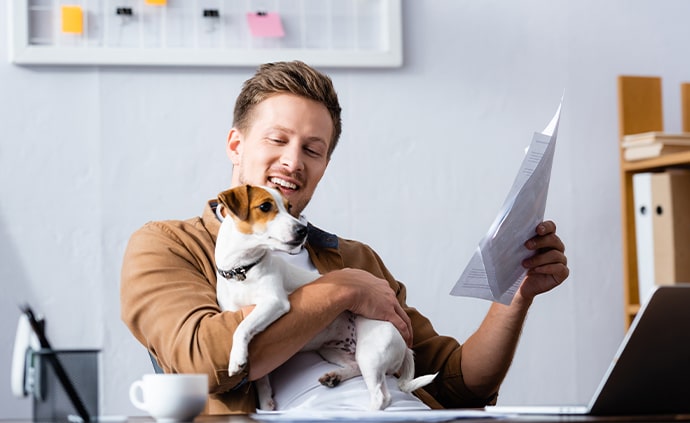 man sitting in front of laptop holding small dog 